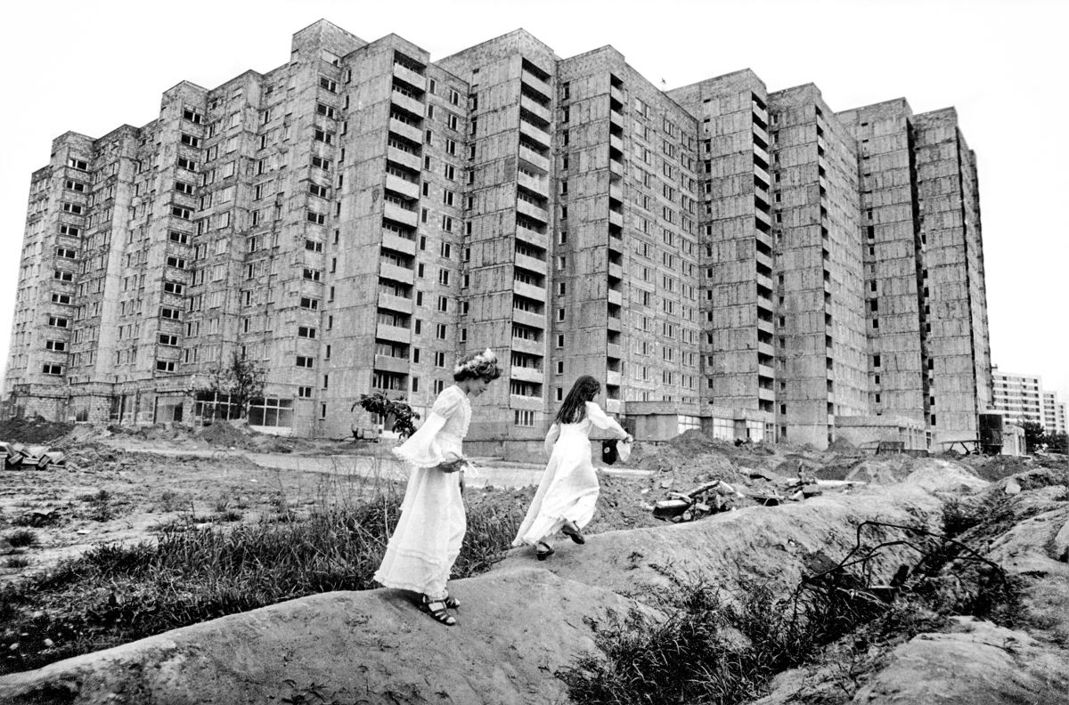 Fotografia czarno-biała. Dwie dziewczynki w strojach komunijnych na tle osiedla blokowego